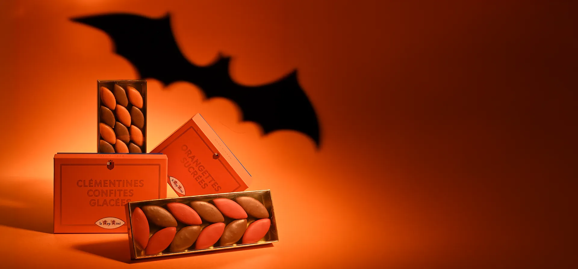 Reglettes de calissons orange, chocolat noisette, cointreau et chocolat noix avec boite d'orangettes sucrées et clémentines glacées avec chauve-sourie sur fond orange halloween.