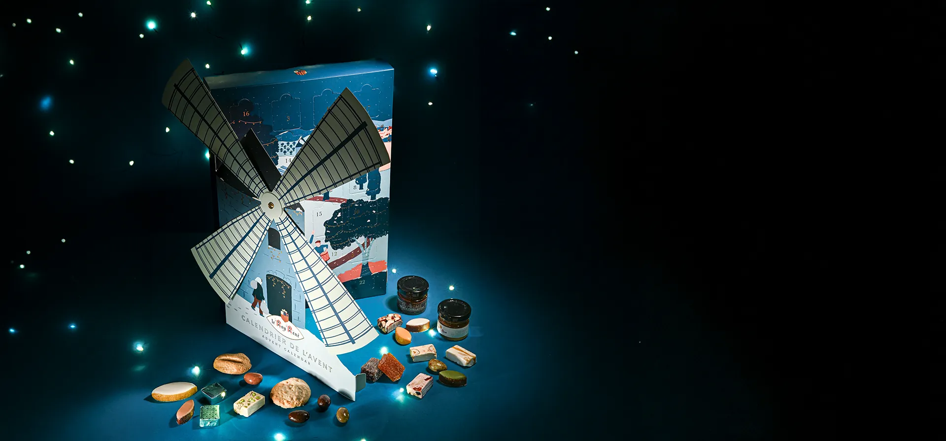 Advent calendar featuring a windmill with outstretched wings and sweets arranged in front, set against a blue background with little Christmas lights.